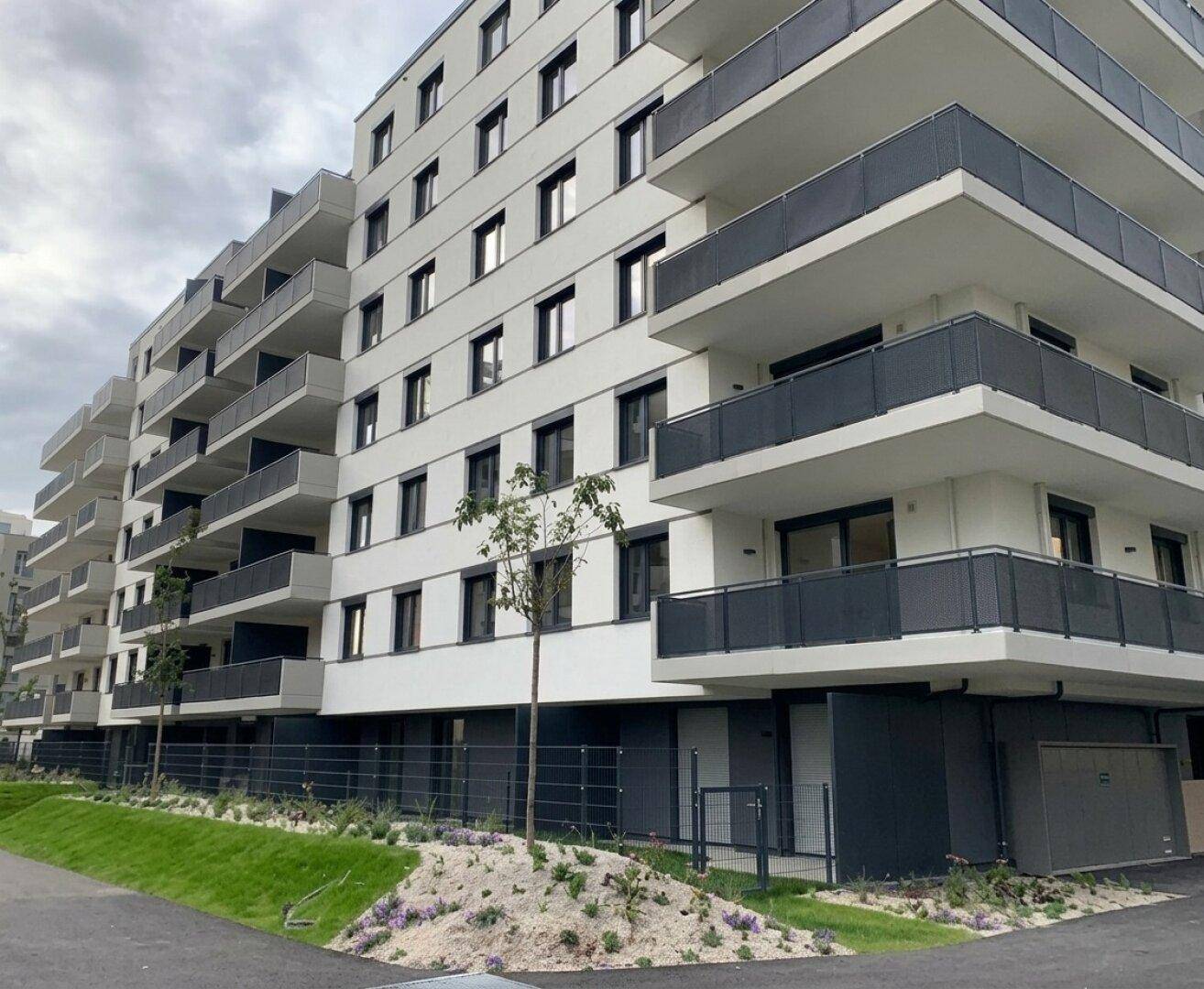 Moderne Wohnanlage mit zahlreichen Balkonen und einer hellen Fassade unter bewölktem Himmel.