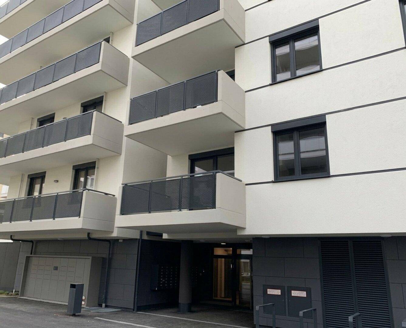 Eingangsbereich eines modernen Wohngebäudes mit Balkonen und dunklen Akzenten an der Fassade.