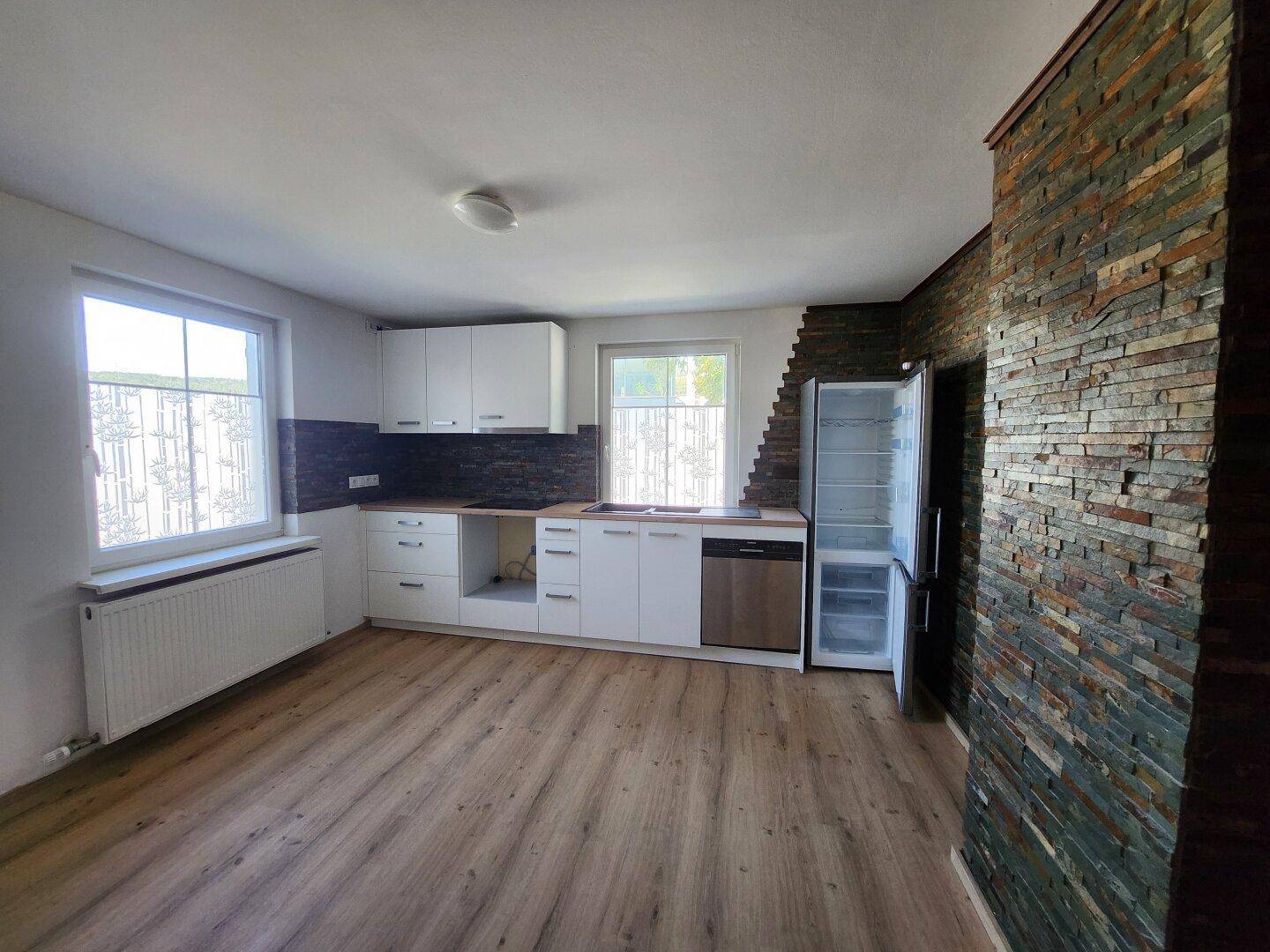 Offene Küche mit moderner Ausstattung, Laminatboden und dekorativer Steinwand als Akzent.