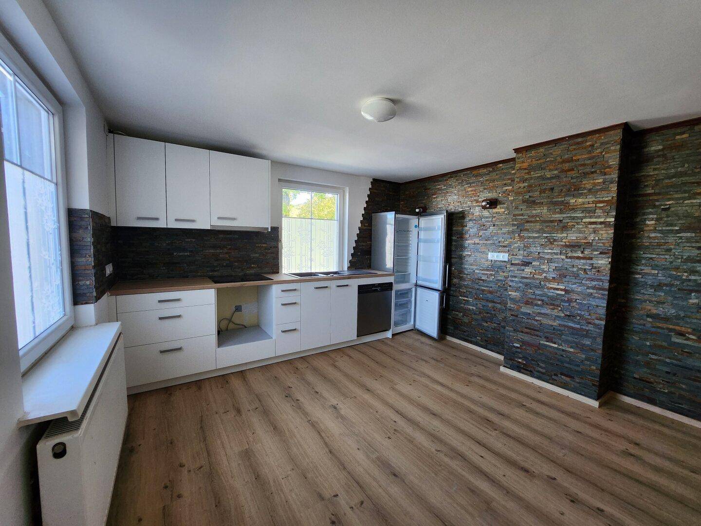 Funktionale Küche mit hellen Schränken, Laminatboden und Heizkörper unter dem Fenster.