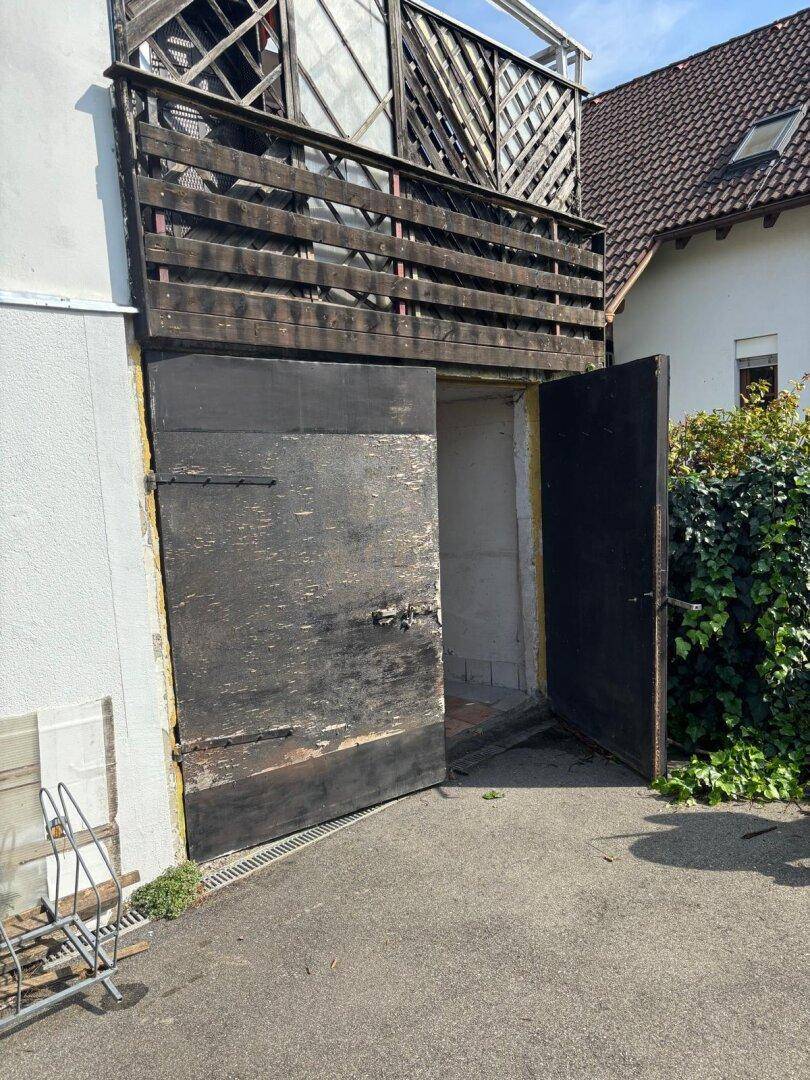 Alte Holztüren führen in das Gebäude, darüber befindet sich ein hölzerner Balkon.