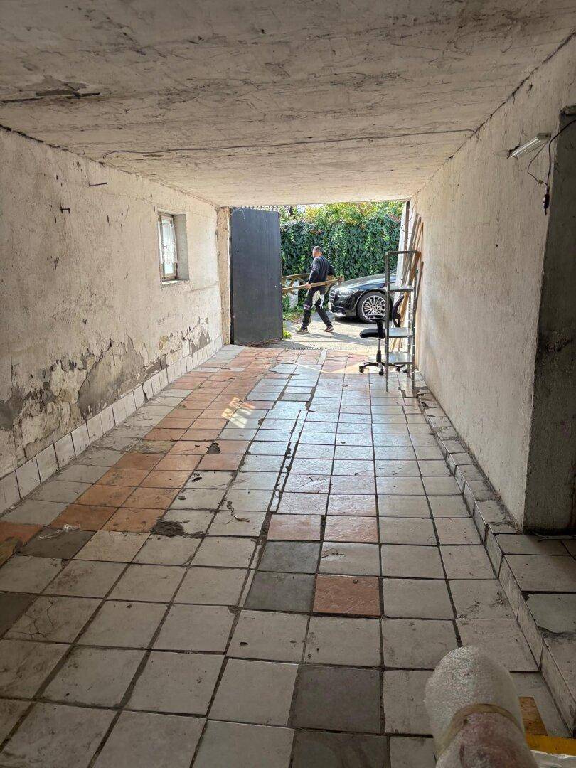 Langer, schmaler Raum mit gefliestem Boden und Betonwänden, der als Garage dient.