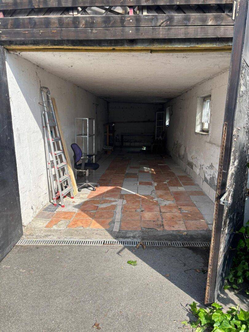 Leere Garage mit gefliestem Boden und Betonwänden, bereit zur Nutzung.