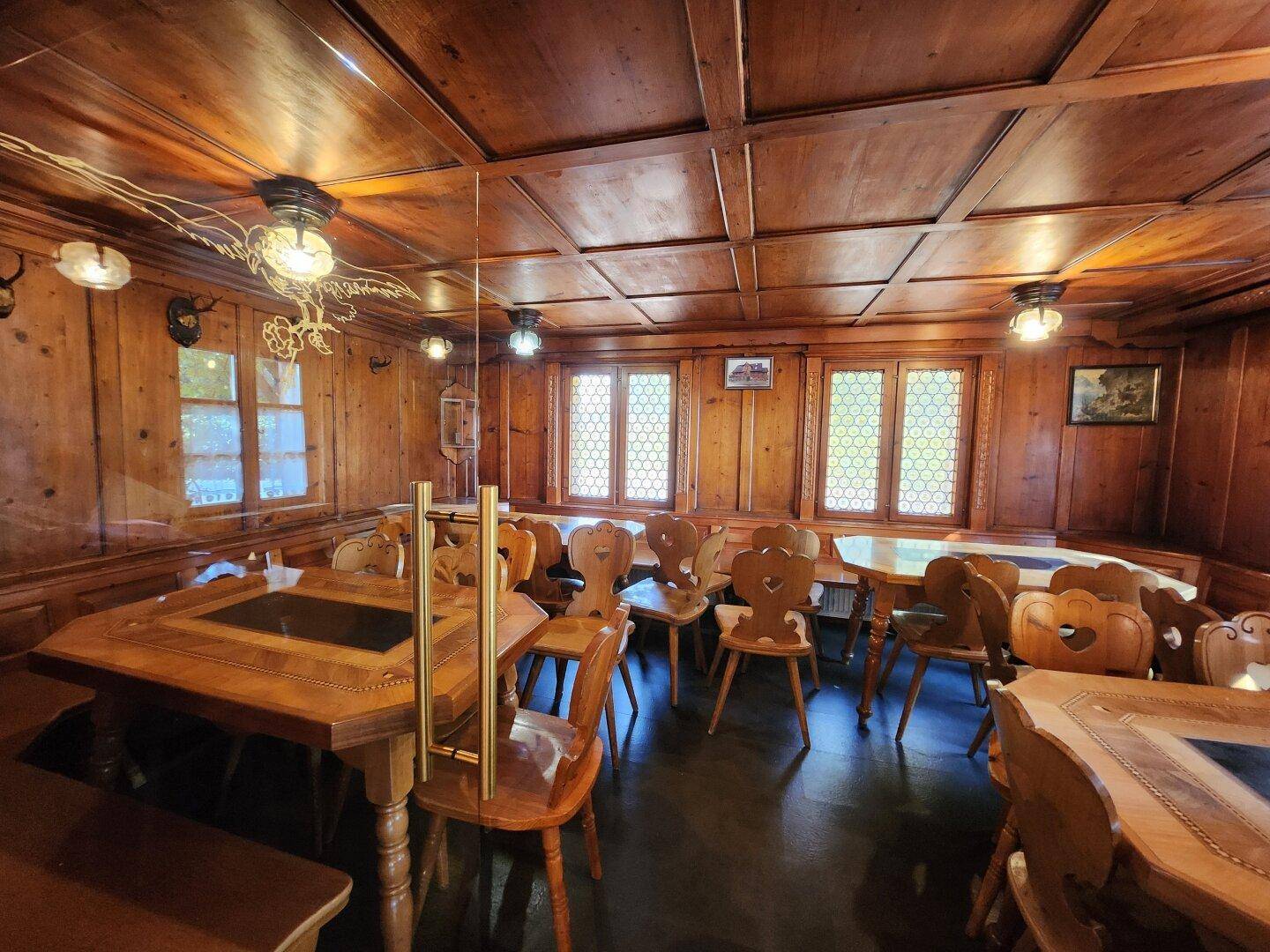 Dunklerer Gastraum mit Holztäfelung und traditionellen Holzmöbeln, mit dekorativen Fenstern.