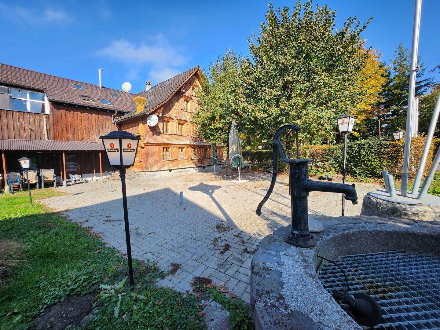 Außenbereich mit altem Brunnen, Laternen und einem traditionellen Gebäude im Hintergrund.