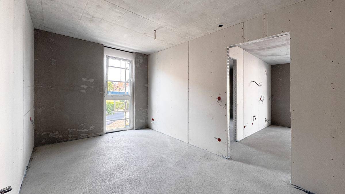Unfertiger Innenraum im Rohbau mit Betonflächen, Trockenbauwänden und einem Fenster.