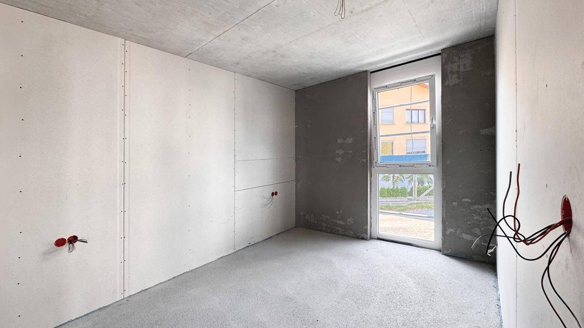 Unfertiger Innenraum im Rohbau mit Betonflächen, Trockenbauwänden und einem Fenster.