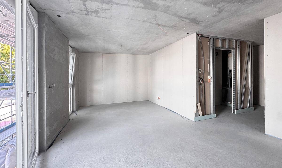 Unfertiger Innenraum im Rohbau mit Betonflächen, Trockenbauwänden und Zugang zur Baustelle.