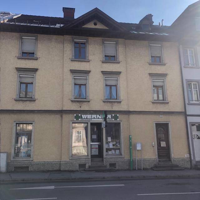 Vorderansicht eines historischen Gebäudes mit einer Apotheke im Erdgeschoss und geschlossenen Rollläden.