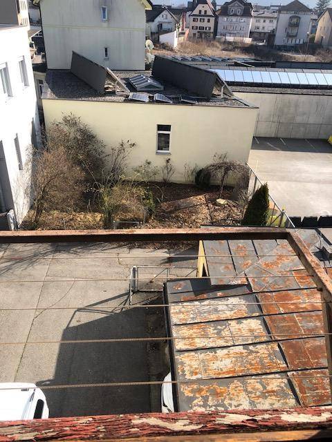 Blick von oben auf einen Hinterhof mit einem kleinen Gartenbereich, umliegenden Gebäuden und Solarpaneelen auf einem Dach.