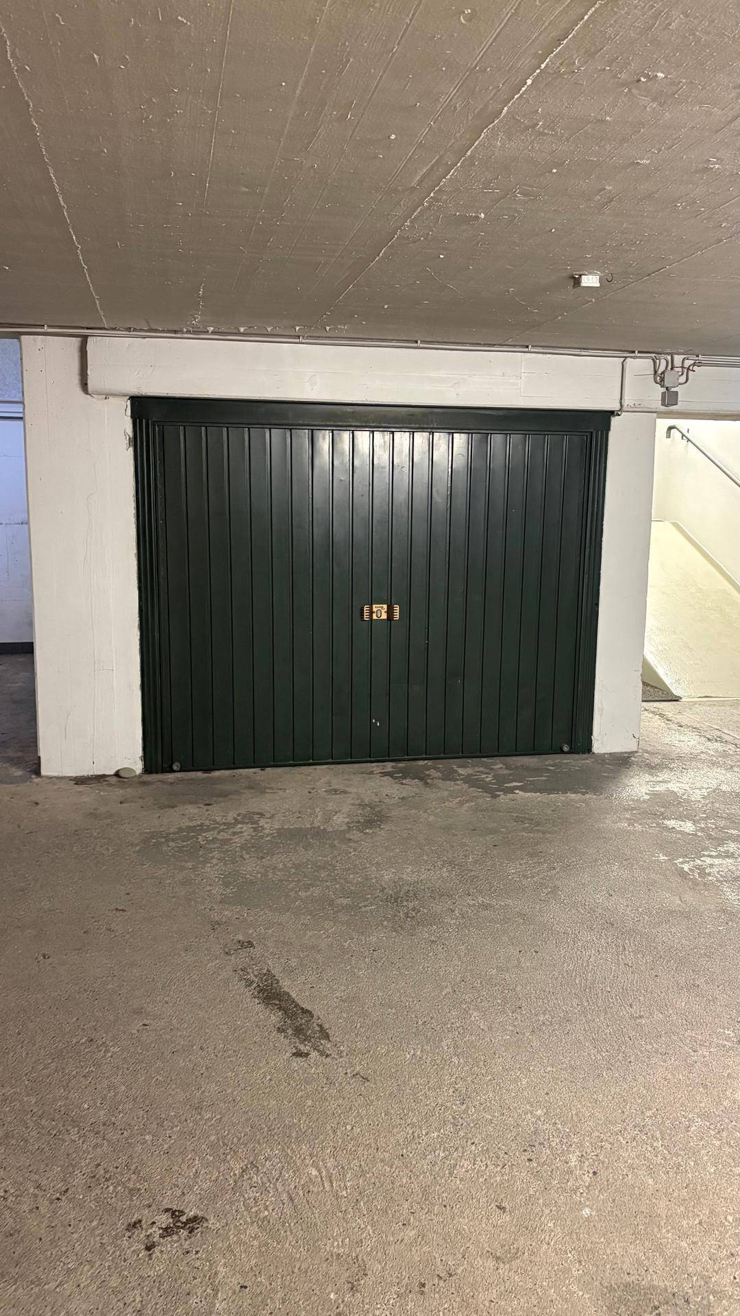 Dunkelgrünes Garagentor in einer Tiefgarage mit Betonboden und -decke.