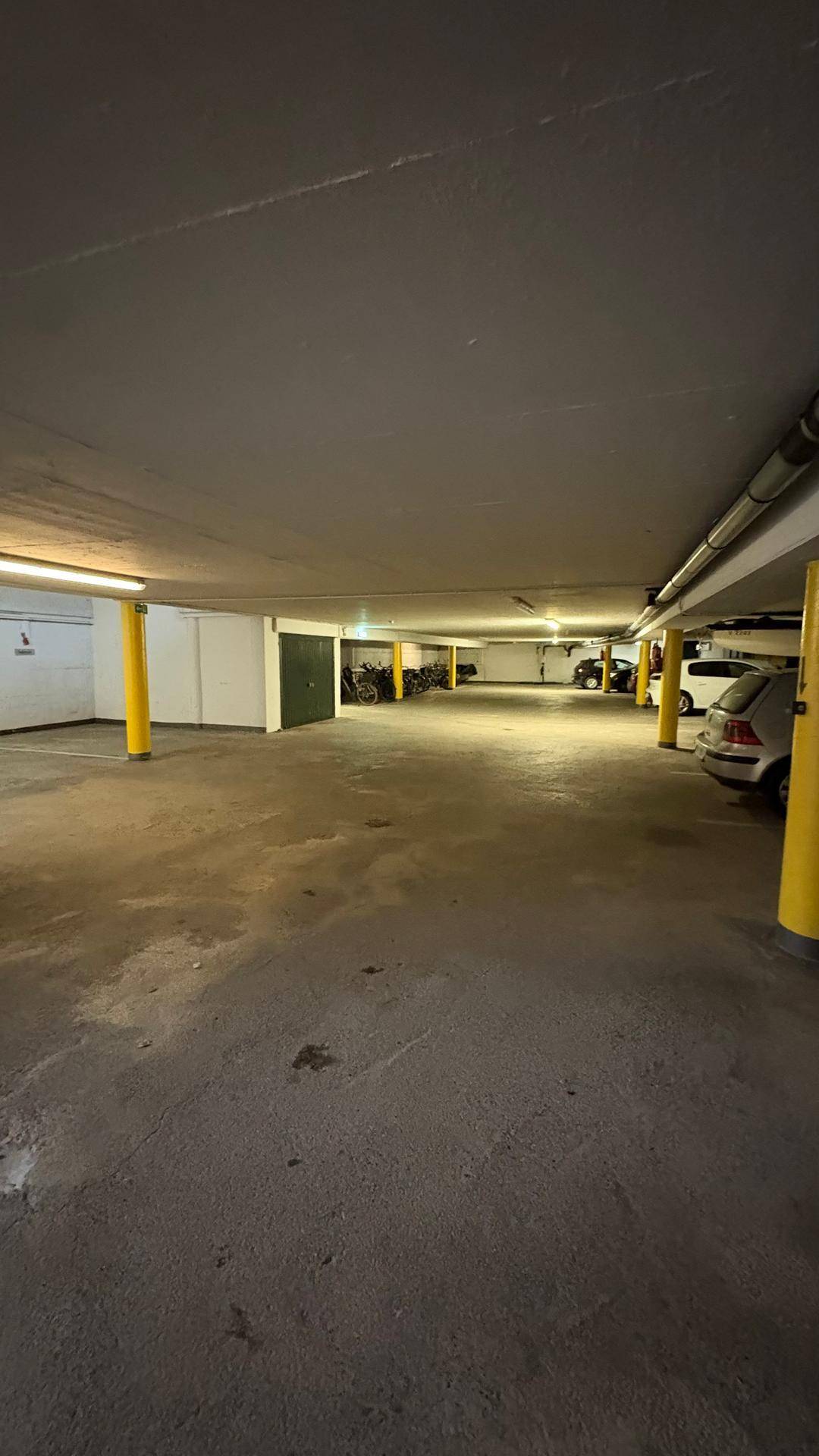 Geräumige Tiefgarage mit gelben Säulen und mehreren Stellplätzen für Fahrzeuge.