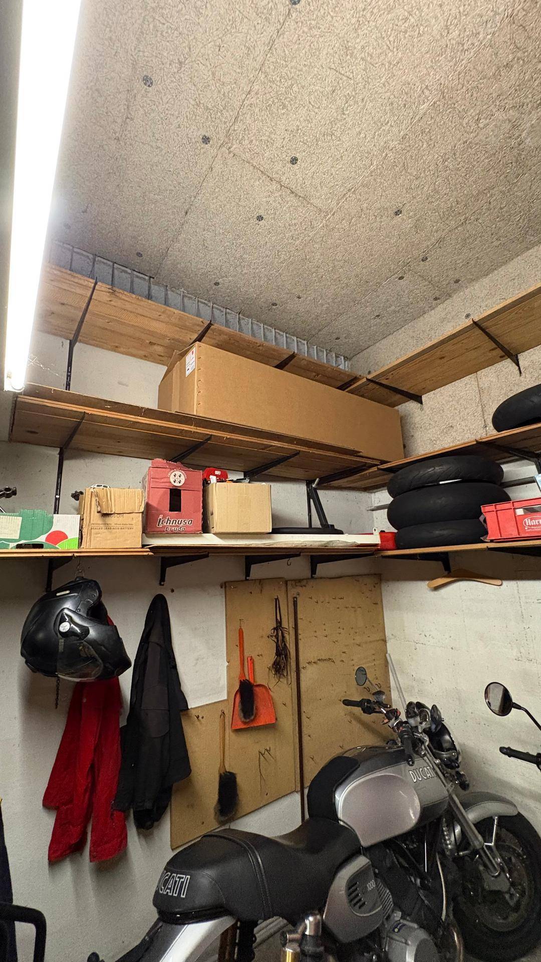 Abstellraum mit Holzregalen, Motorrad und verschiedenen Lagergegenständen.