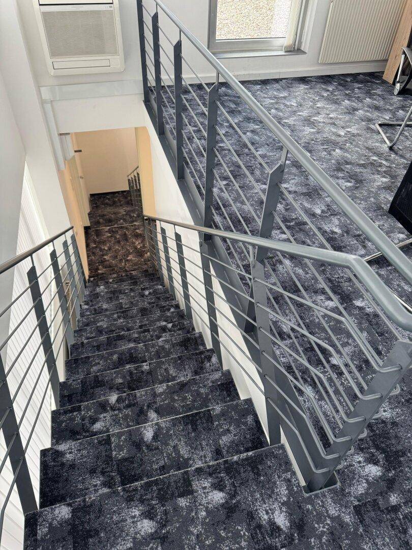Innenansicht eines Treppenhauses mit modernem Teppichboden und Metallgeländer.