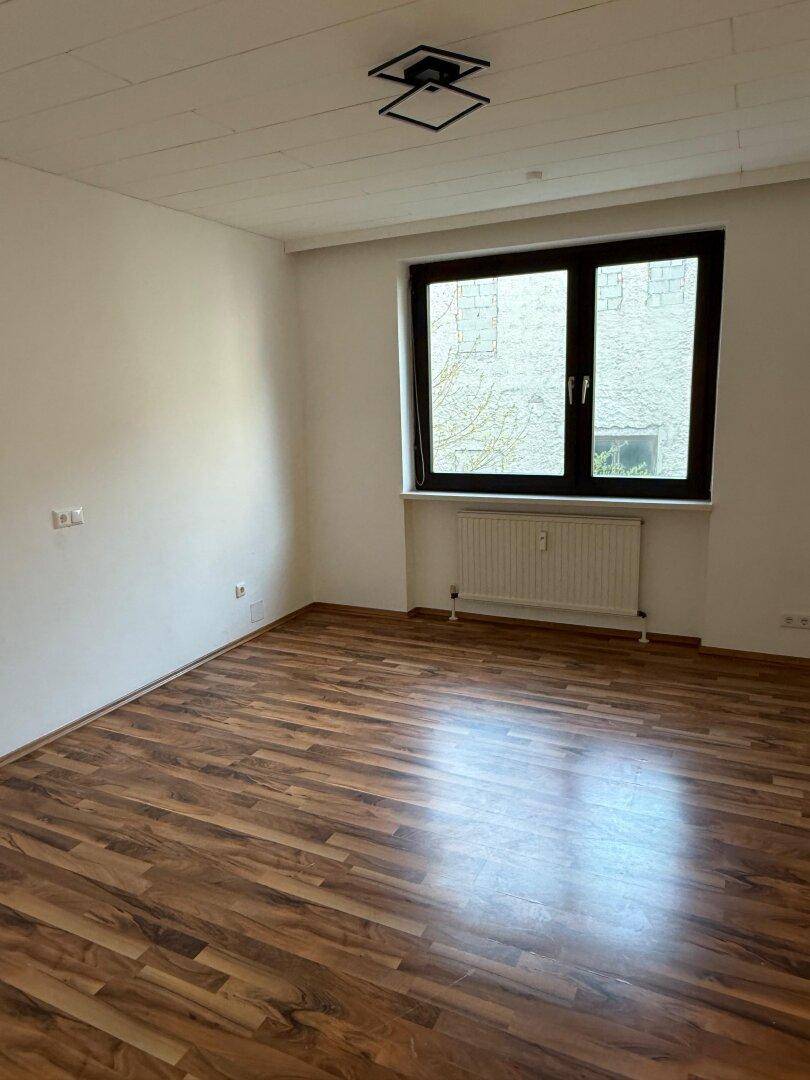 Leeres Schlafzimmer mit Laminatboden und einem großen Fenster, das viel Tageslicht hereinlässt.