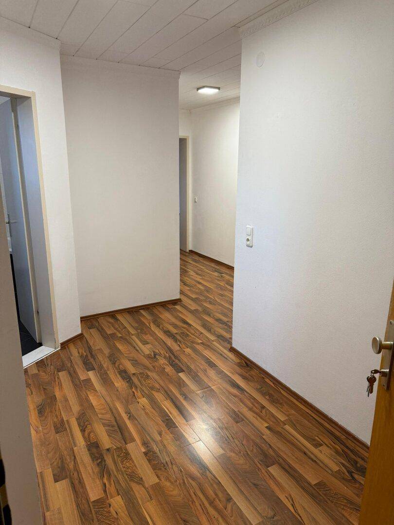 Heller Flur mit Laminatboden und weißen Wänden, der zu weiteren Räumen führt.