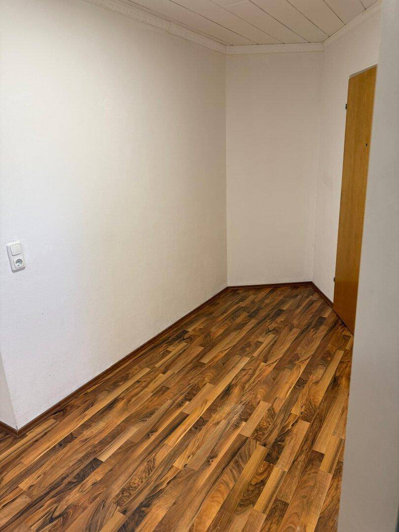 Kleiner, leerer Raum mit Laminatboden und weißen Wänden, vielseitig nutzbar.