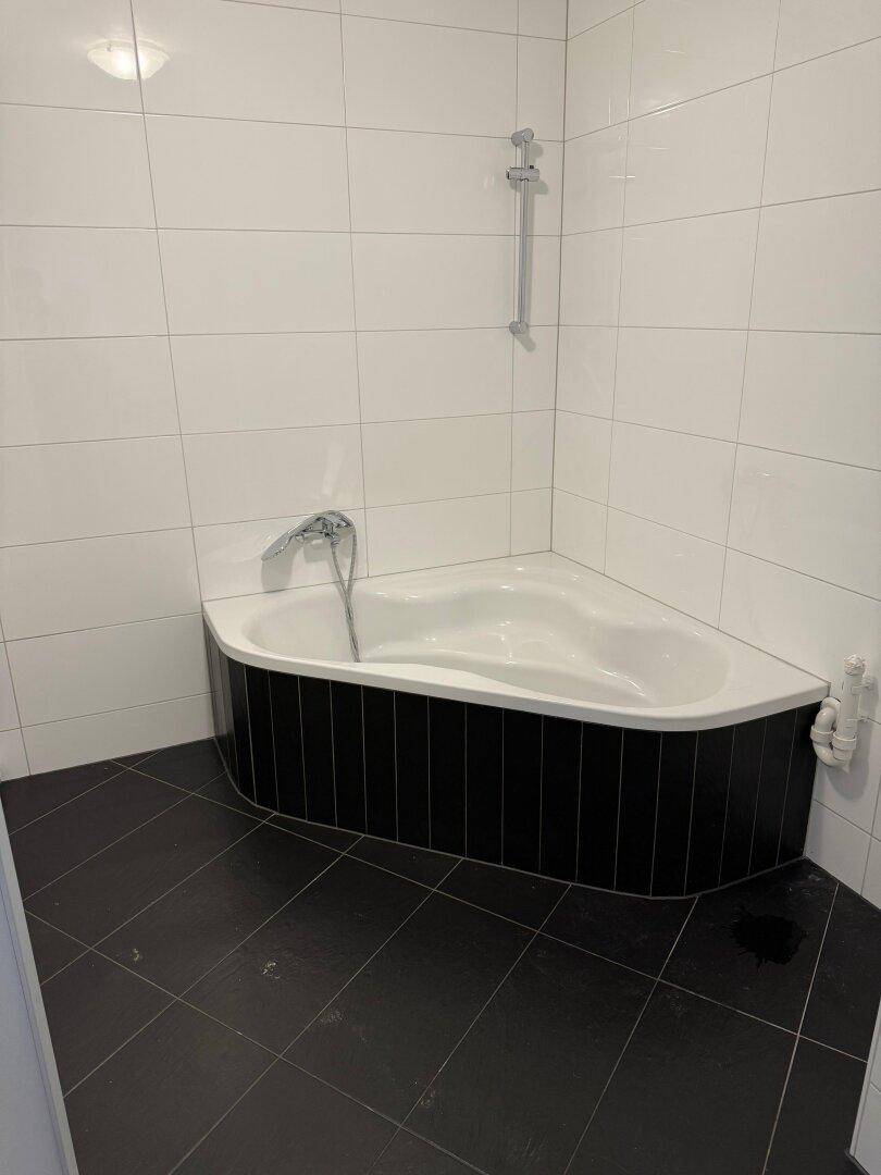 Modernes Badezimmer mit schwarzen Bodenfliesen und einer weißen Eckbadewanne.
