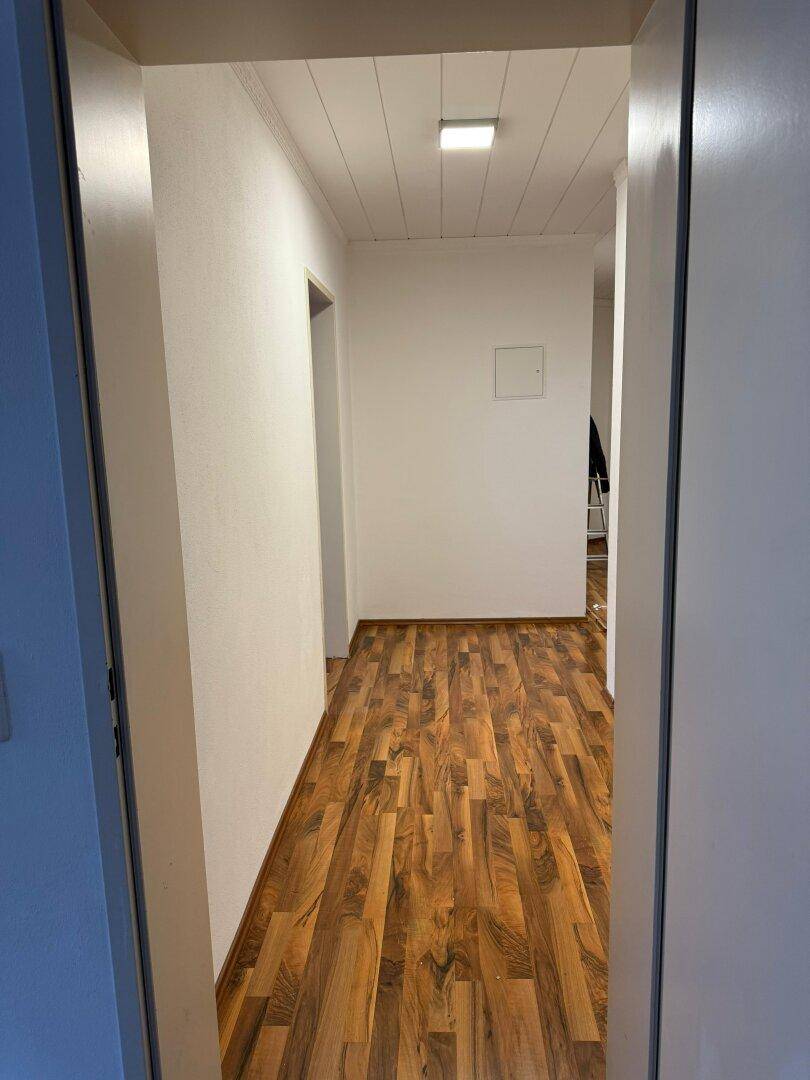 Langer, heller Flur mit Laminatboden und weißen Wänden, der die verschiedenen Bereiche verbindet.