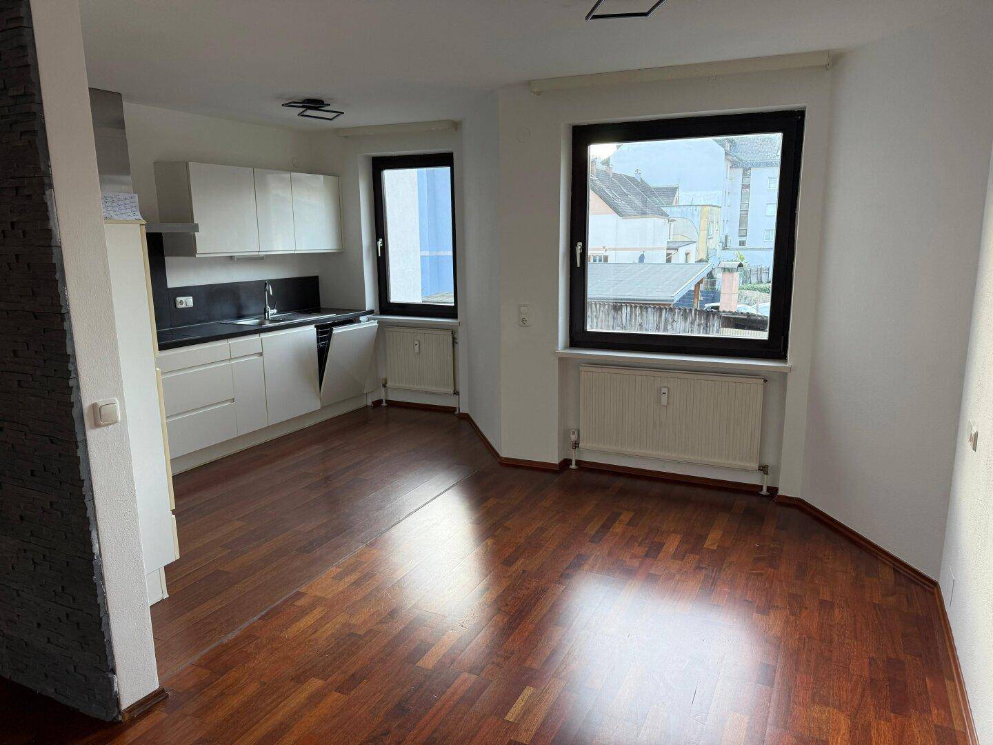 Offener Wohnbereich mit integrierter weißer Küche und Blick auf die Umgebung durch große Fenster.