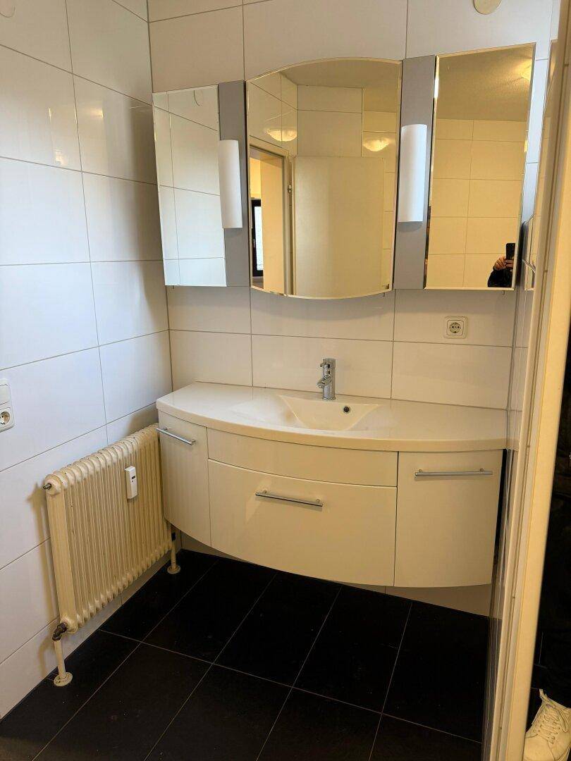 Badezimmer mit modernem Waschtischunterschrank, Spiegel und weißen Wandfliesen.