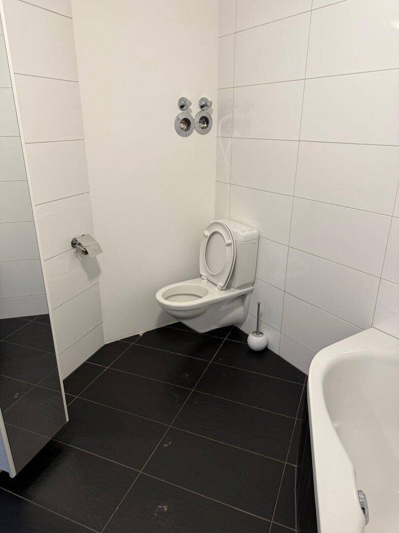 Helles WC mit wandhängender Toilette und schwarzen Bodenfliesen, sauber und funktional.