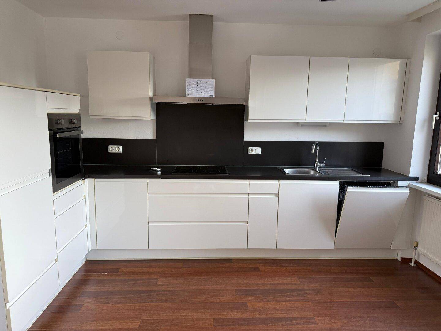 Moderne Einbauküche mit weißen Hochglanzfronten, dunkler Arbeitsplatte und integrierten Geräten.