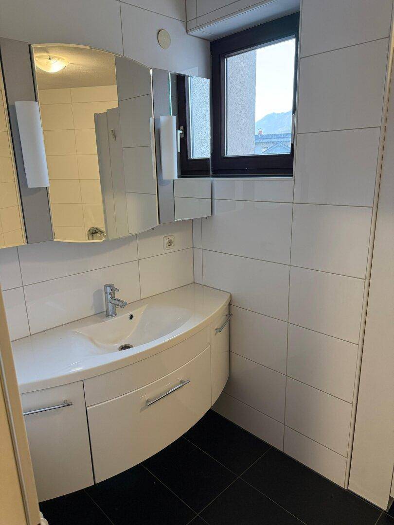 Badezimmer mit Waschtisch, Spiegelschrank und Fenster für natürliche Belüftung und Licht.