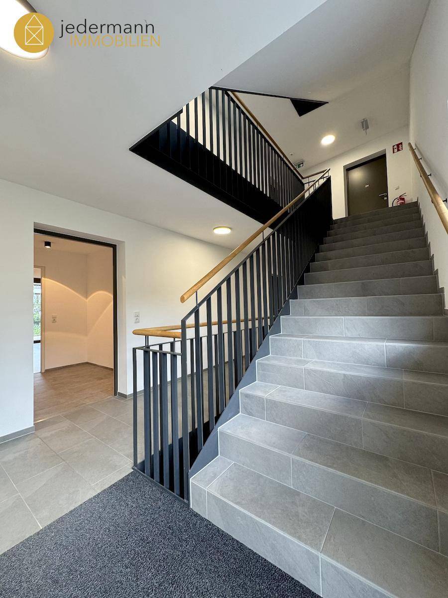 Modernes Treppenhaus mit elegantem Geländer und Fliesenboden in einem Mehrfamilienhaus.