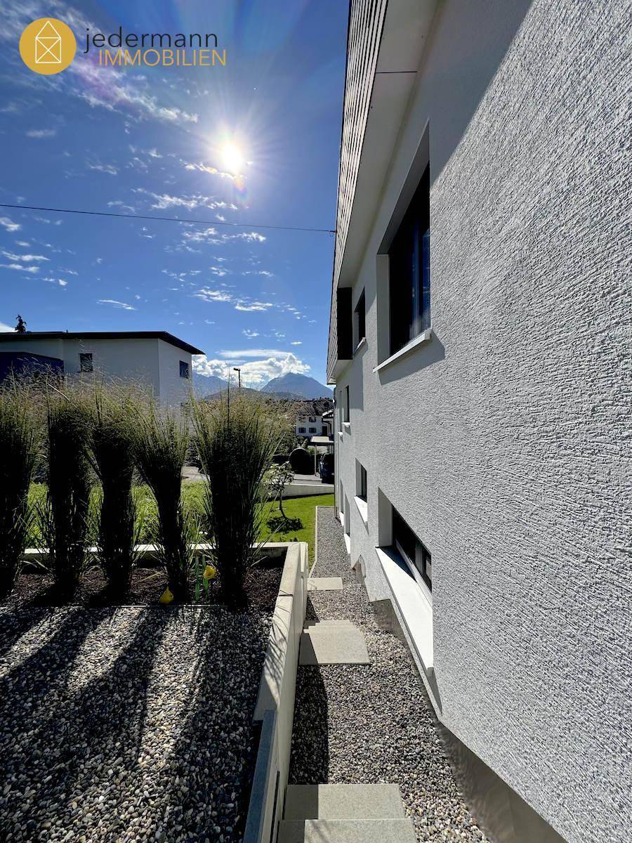 Moderne Hausfassade mit Kiesweg und Bepflanzung unter strahlendem Himmel.