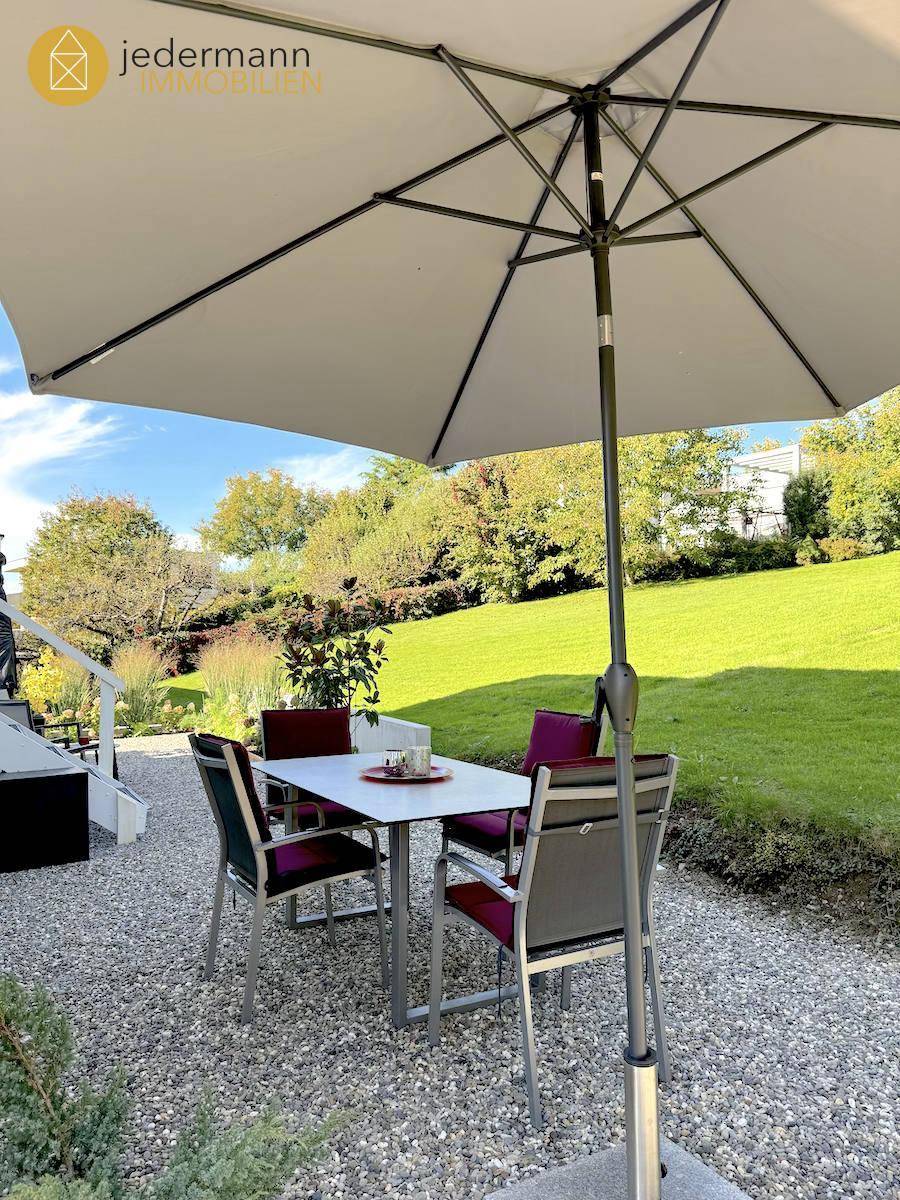 Gemütliche Terrasse mit Esstisch, Stühlen und Sonnenschirm im Grünen.
