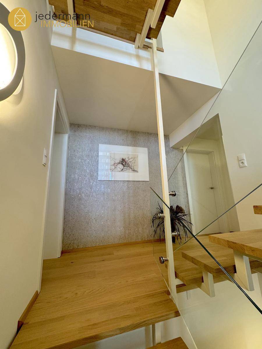 Moderner Flur mit Holzfußboden und Treppenaufgang mit Glasgeländer.