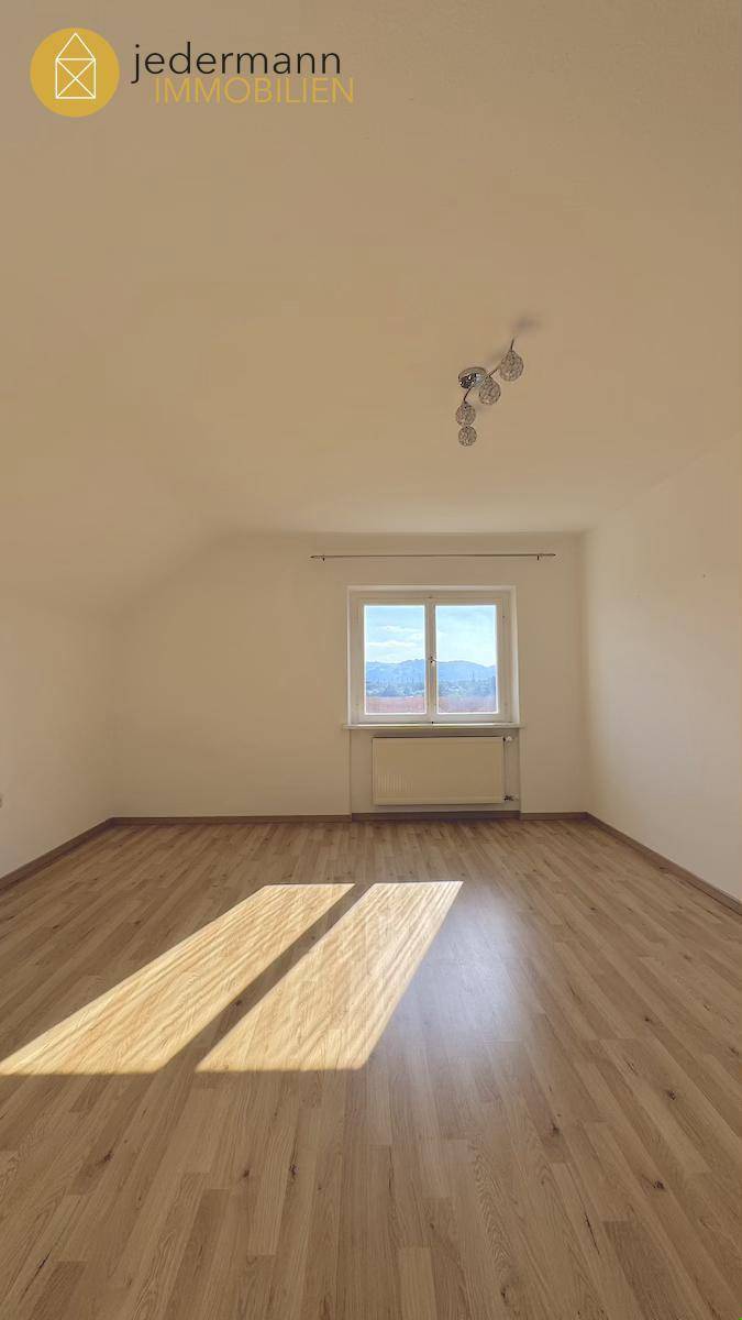 Helles Zimmer mit Laminatboden und einem Fenster, das viel Sonnenlicht hereinlässt.