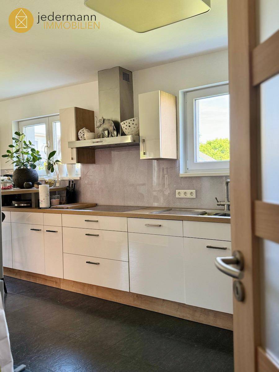 Moderne Küche mit weißen Hochglanzfronten, Holz-Arbeitsplatte und Fenster für Tageslicht.