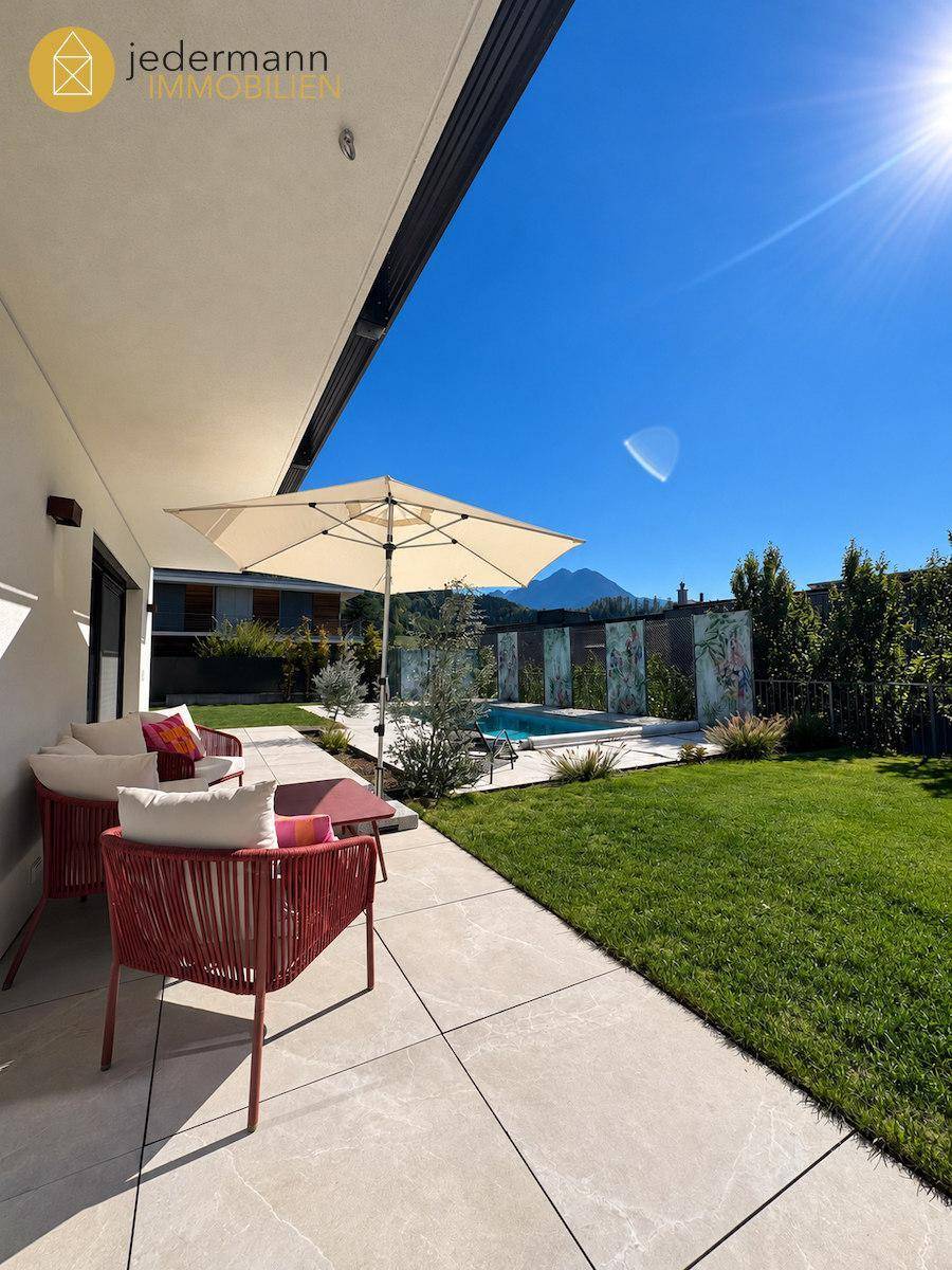 Sonnenterrasse mit Sitzgelegenheiten, Sonnenschirm und Blick auf den Pool und die Berge.