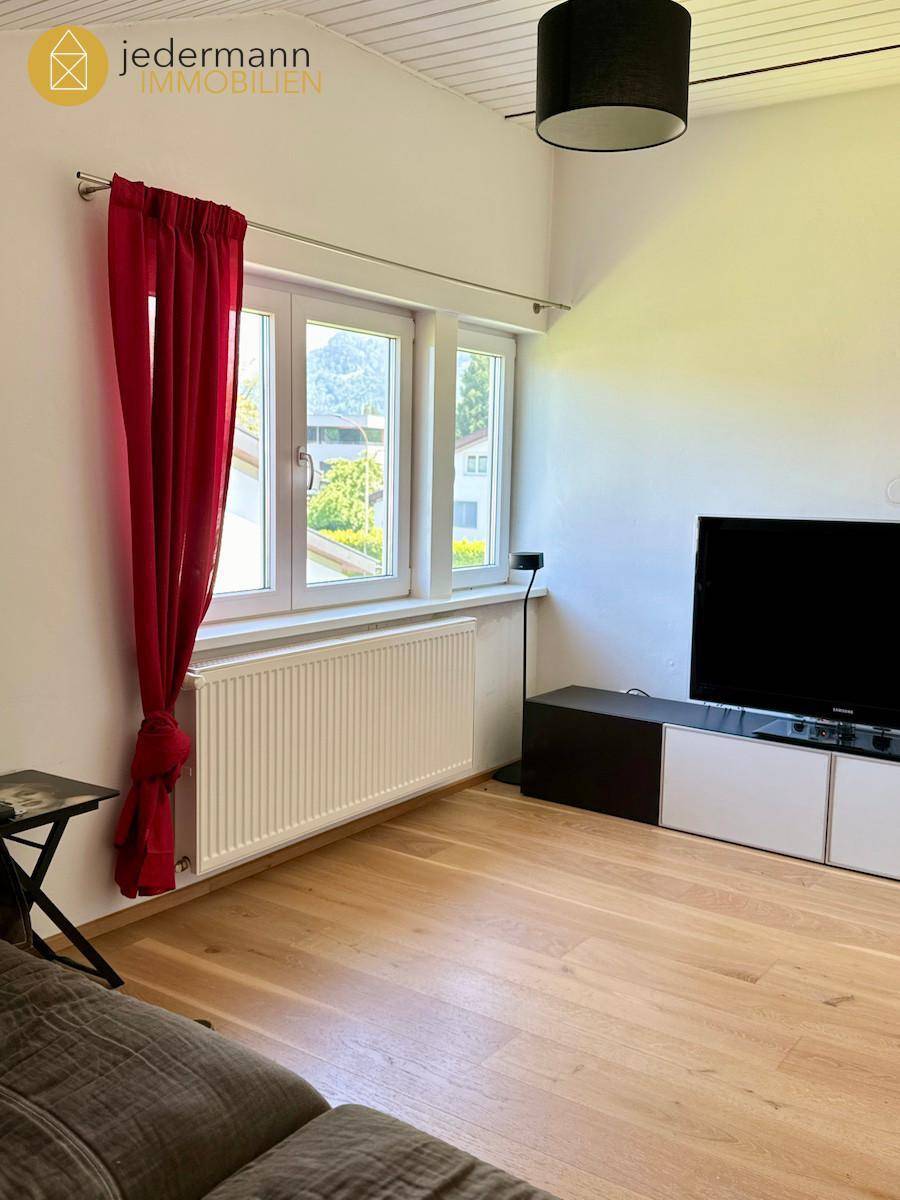 Gemütliches Wohnzimmer mit Parkettboden, Fernseher und Fenster mit roten Vorhängen.