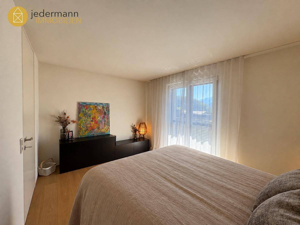 Helles Schlafzimmer mit Holzboden, Einbauschränken und Zugang zum Balkon mit Bergblick.