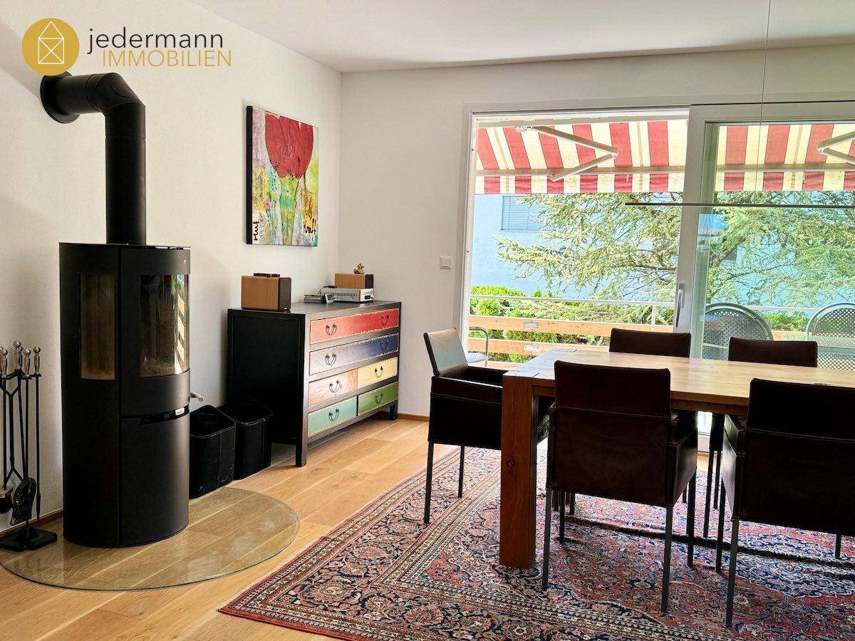 Gemütlicher Essbereich mit Holztisch, Kaminofen und Zugang zu einem Balkon mit Markise.