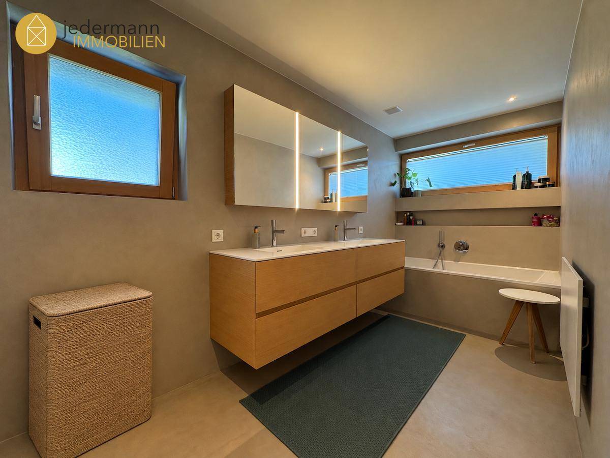 Modernes Badezimmer mit Doppelwaschbecken, Badewanne und zwei Fenstern.