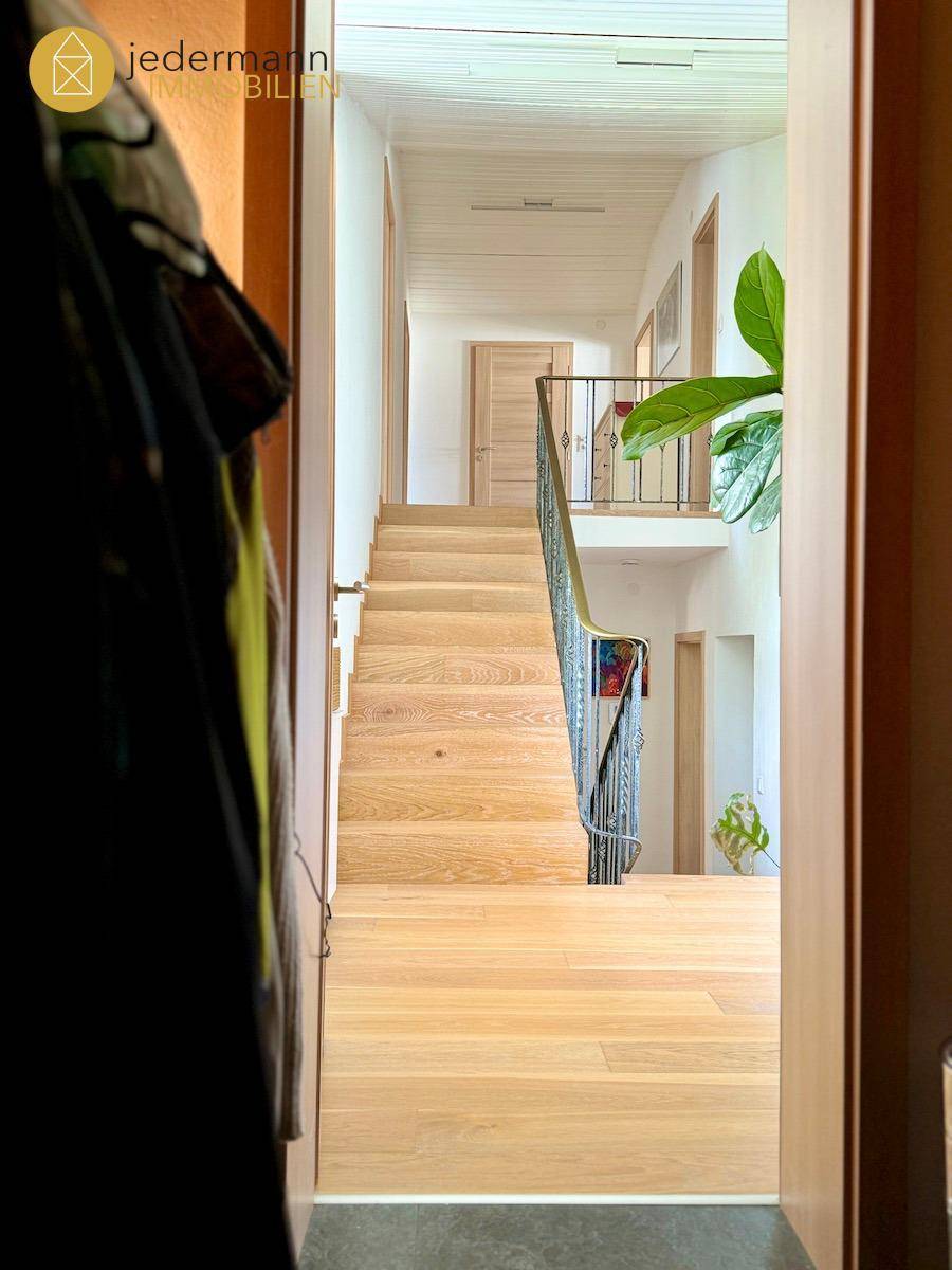 Heller Flur mit Holztreppe und schmiedeeisernem Geländer, der die Etagen verbindet.