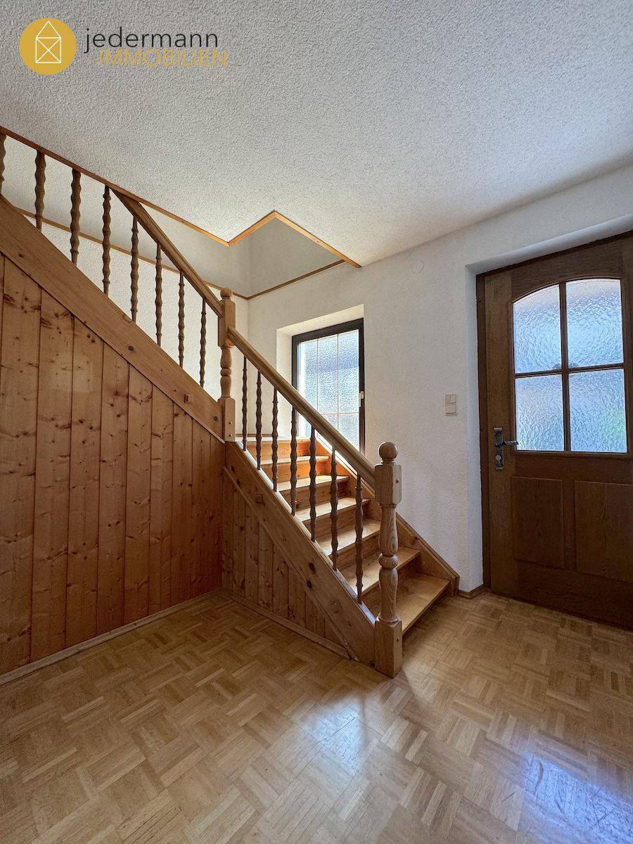 Eingangsbereich mit Holztreppe, Holzvertäfelung und Parkettboden, der in die oberen Etagen führt.