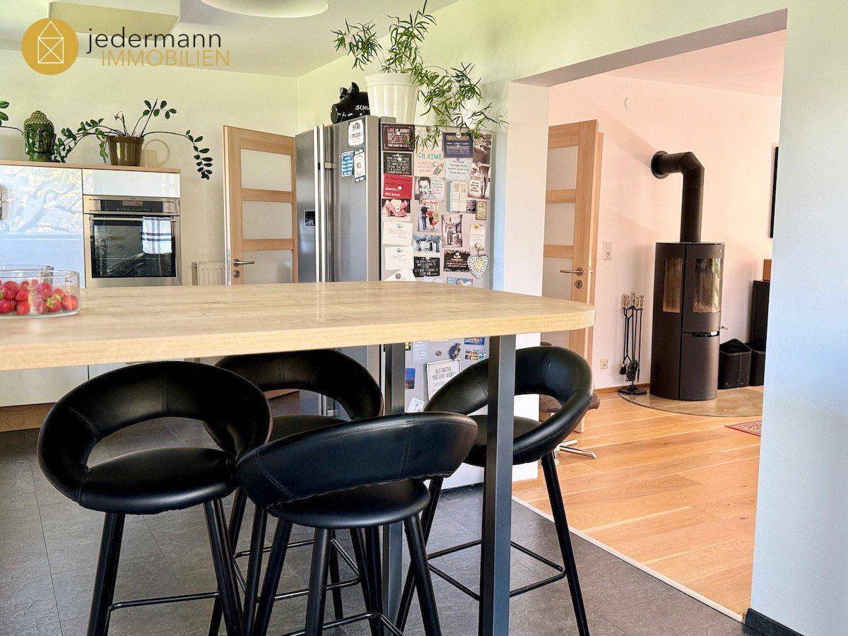 Offene Küche mit Frühstücksbar, modernen Geräten und Blick in den Wohnbereich mit Kamin.