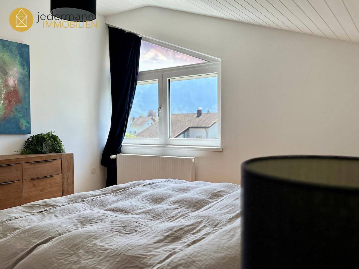 Schlafzimmer mit schrägen Wänden, großem Fenster und Blick auf die umliegenden Dächer.