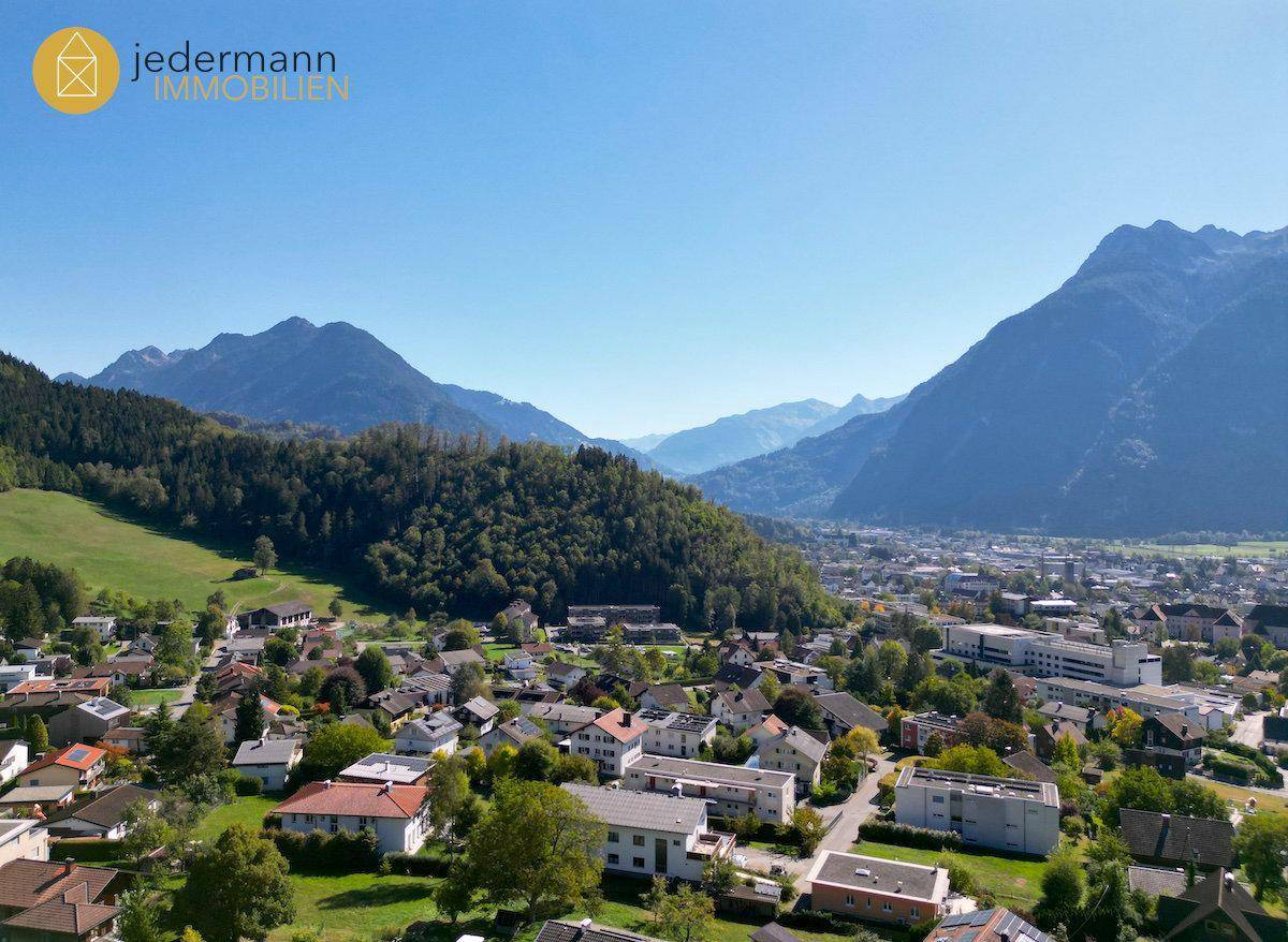 Weitläufiger Blick über eine Stadt im Tal, umgeben von grünen Bergen.