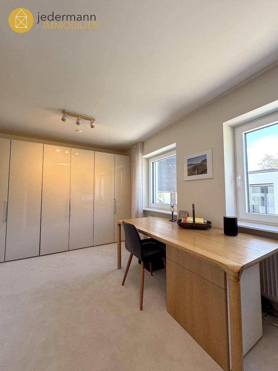 Helles Zimmer mit großem Schreibtisch, Einbauschränken und Teppichboden.