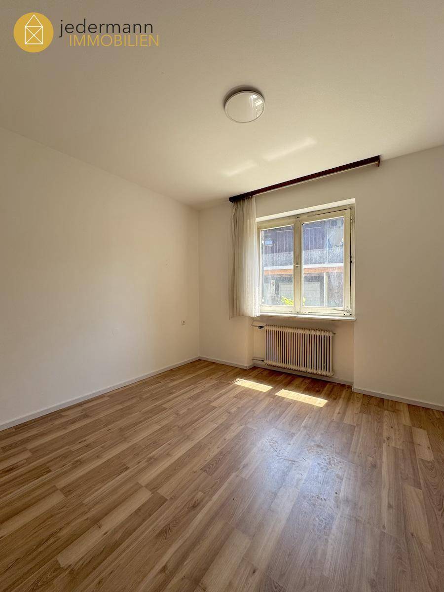 Helles Schlafzimmer mit Holzboden, Fenster und Heizkörper, ideal für ein Kinderzimmer.