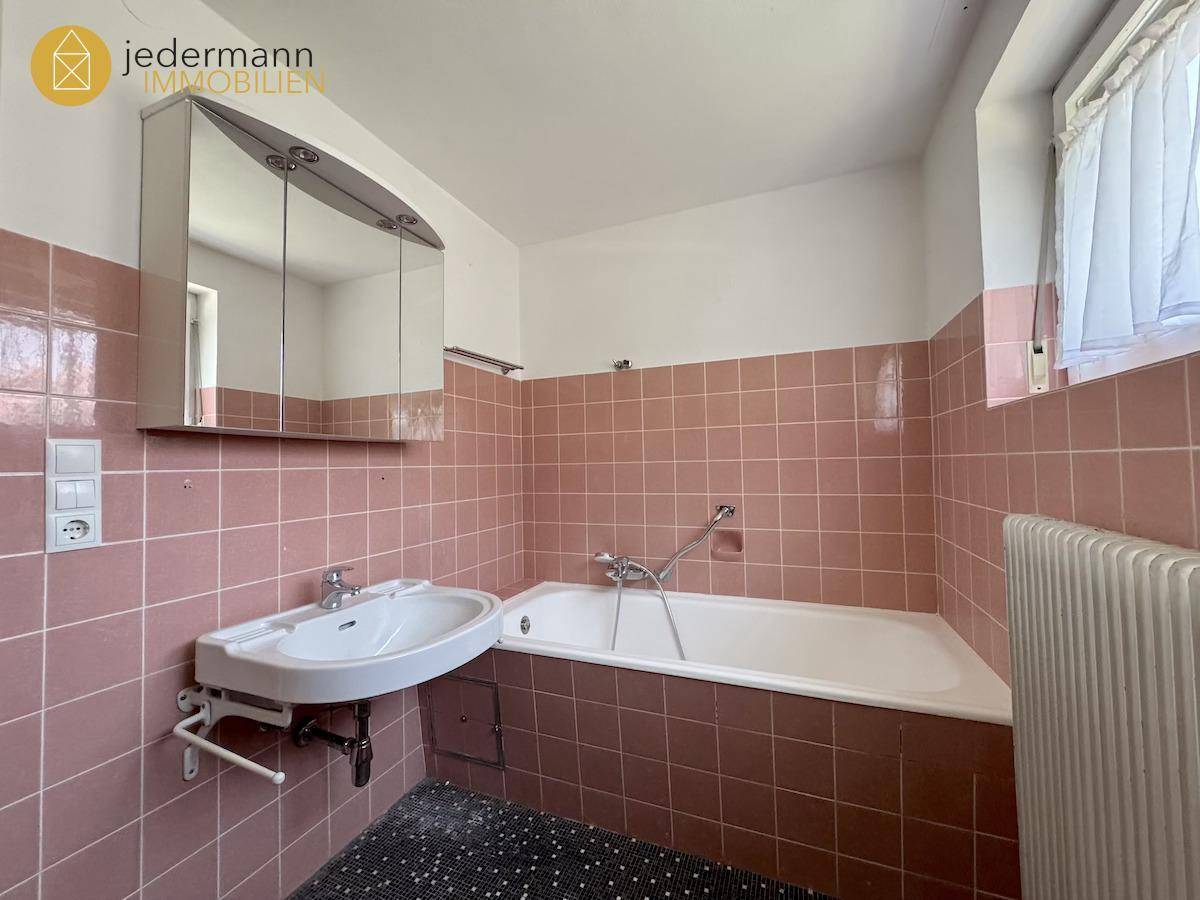 Badezimmer mit rosa Fliesen, Badewanne, Waschbecken und Spiegelschrank.