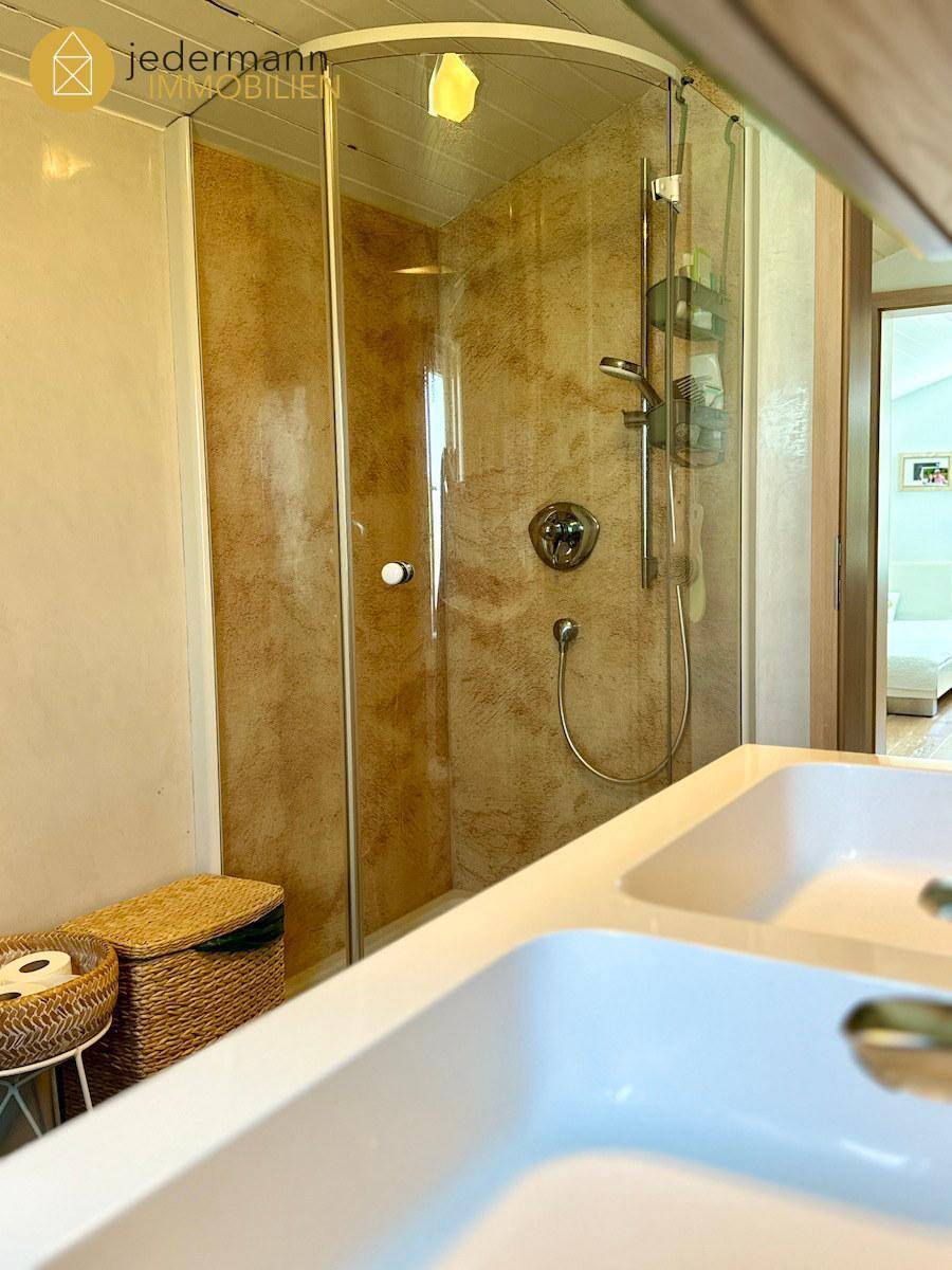 Badezimmer mit Doppelwaschbecken, Duschkabine und hellen Wandfliesen.
