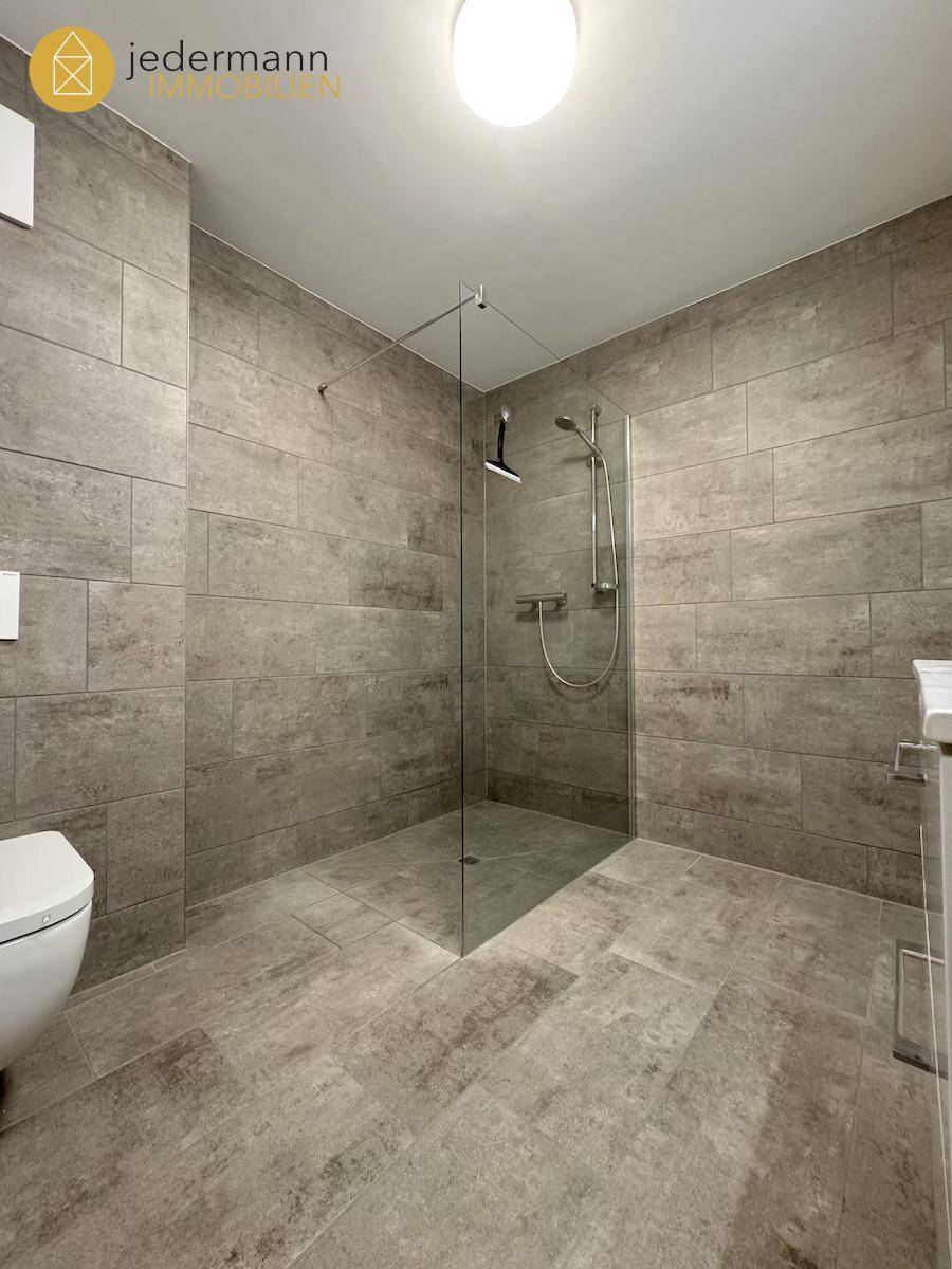 Modernes Badezimmer mit großformatigen grauen Fliesen und ebenerdiger Dusche.