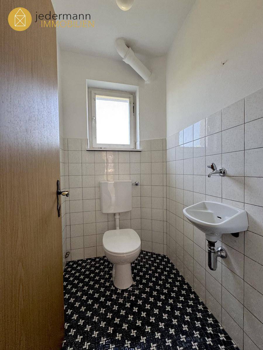 Kleines Gäste-WC mit weißer Toilette, Waschbecken und schwarz-weiß gemustertem Boden.